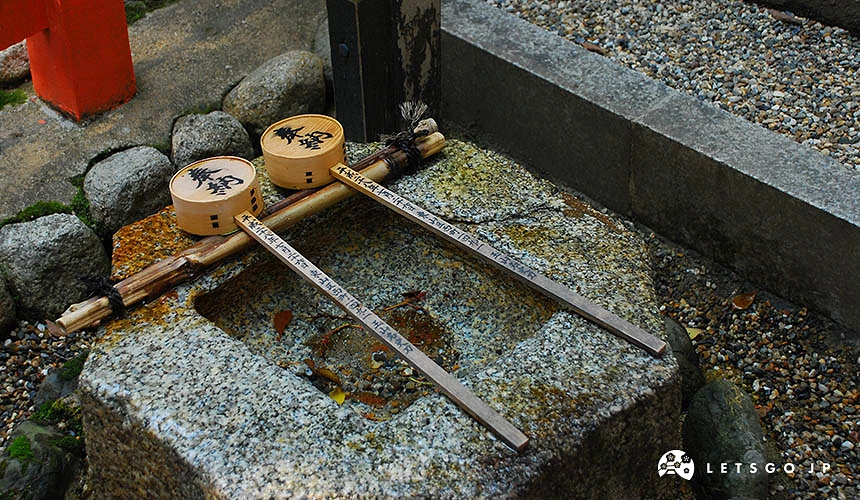 日本神社的手水鉢與木製柄杓。石頭製成的淨手水槽上,橫放著兩把印有「奉納」字樣的木柄水杓。