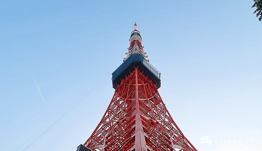 紅白相間的東京鐵塔自地面仰望而上,展現出鋼骨結構的壯麗與對稱之美,搭配晴朗無雲的藍天