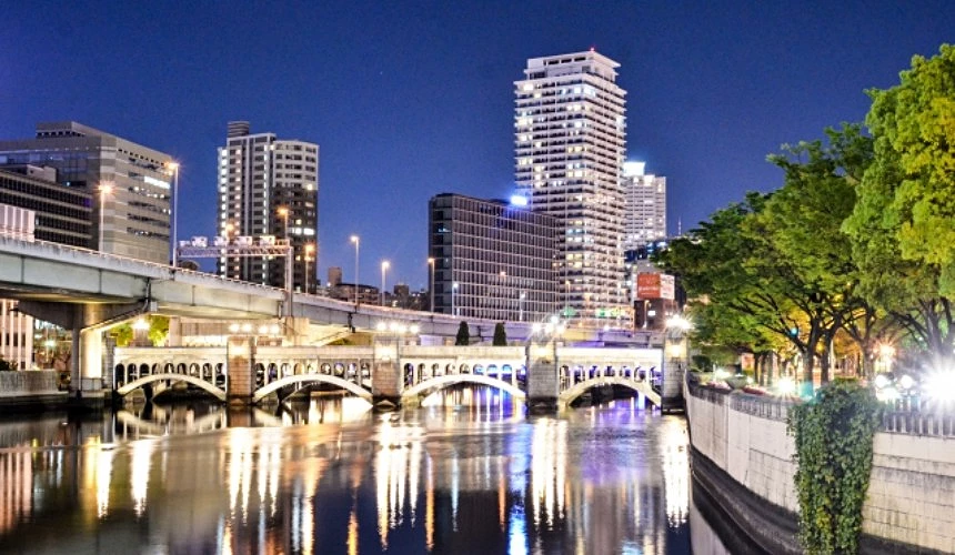 大阪北濱地區夜景,橋樑與高樓倒映於河面,右側綠意盎然的河岸步道展現水都夜晚魅力