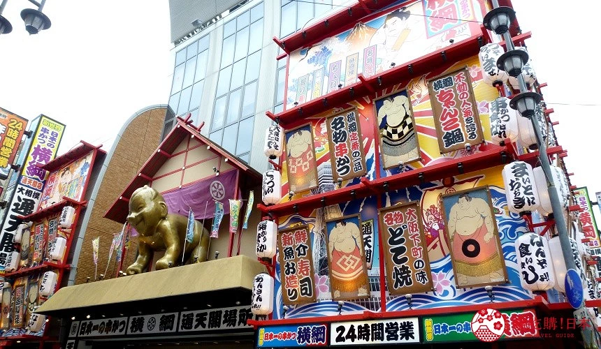 大阪新世界地區的居酒屋外觀,店面裝飾以巨型金色比利肯神像與繽紛日式燈籠招牌,營業時間24小時