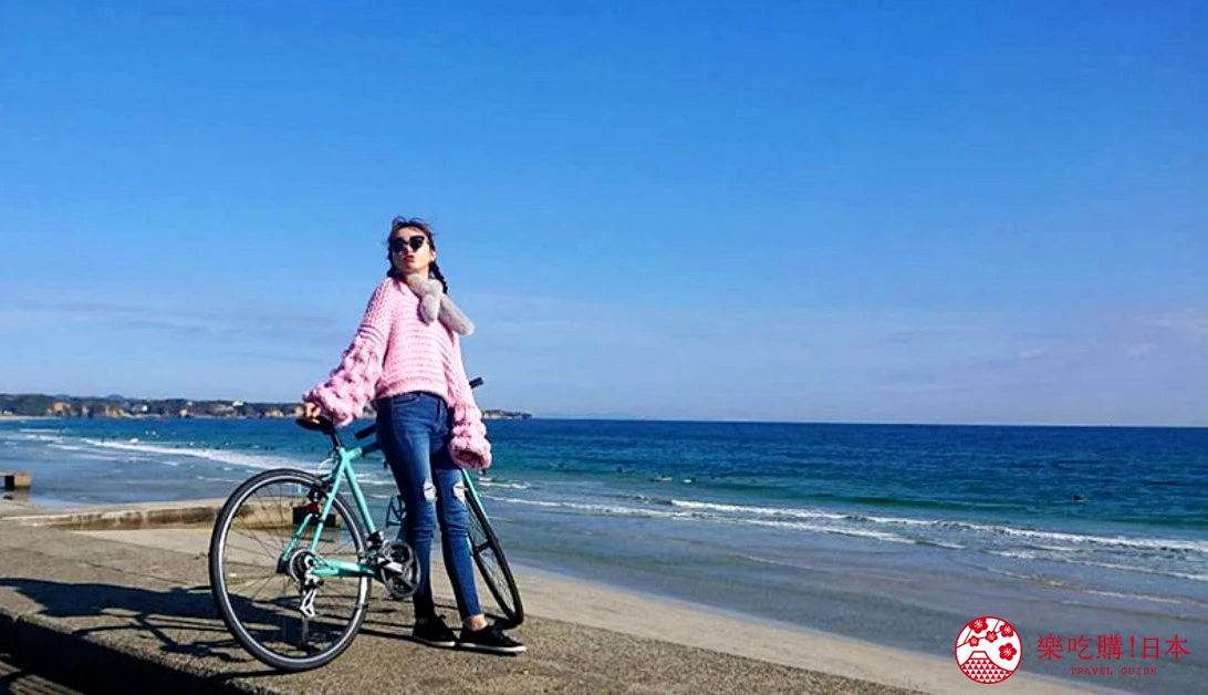 女性騎自行車在海邊,穿粉色上衣戴太陽眼鏡,背景是藍色海洋
