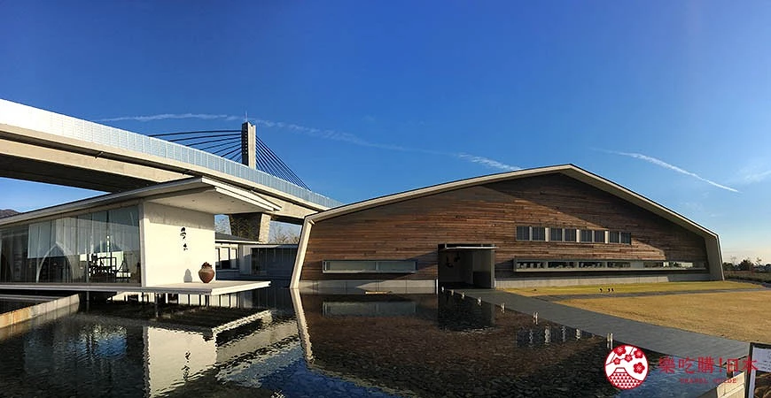 水池環繞的建築群,背景有藍天和橋梁結構