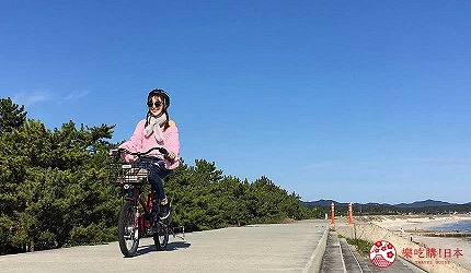女性穿粉色衣服騎自行車在路上,背景是藍天和樹木