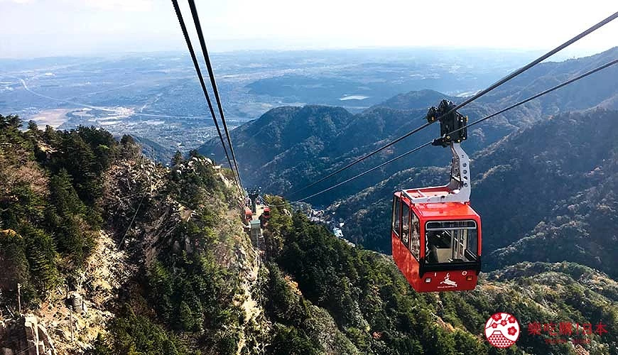 紅色纜車行駛在山區纜線上,背景是層疊山脈和遠方平原