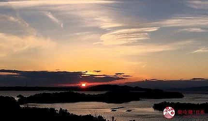 橘紅色太陽在水面上方,天空有雲朵,水中有島嶼