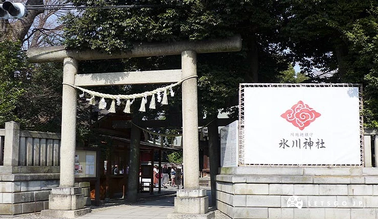 川越冰川神社的鳥居入口,石造鳥居上繫著注連繩,右側設有寫著「川越總鎮守 冰川神社」與神社紋樣的大型白色看板