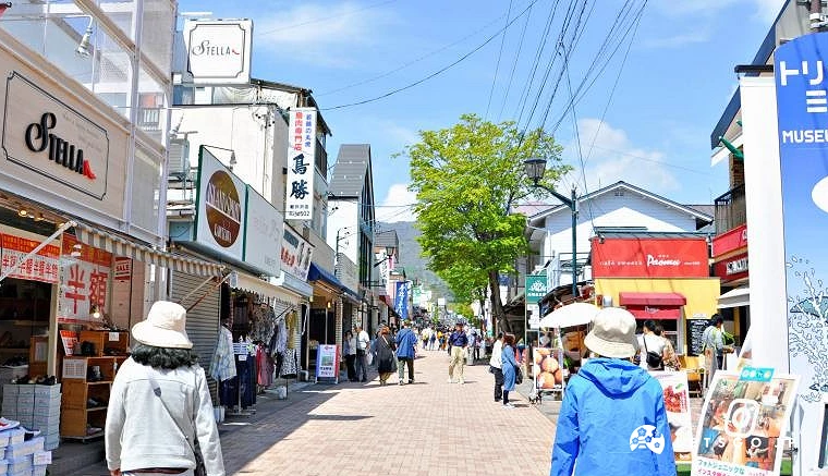 晴天下的舊輕井澤銀座通商店街,兩旁林立特色店鋪與洋風建築,街道上有許多遊客悠閒散步與逛街