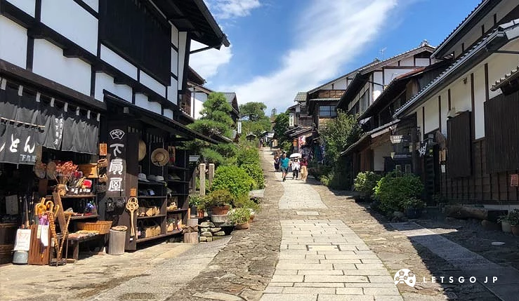 馬籠宿的石板坡道街景,兩側林立著傳統木造建築與店家,旅人走在晴空下的古街中