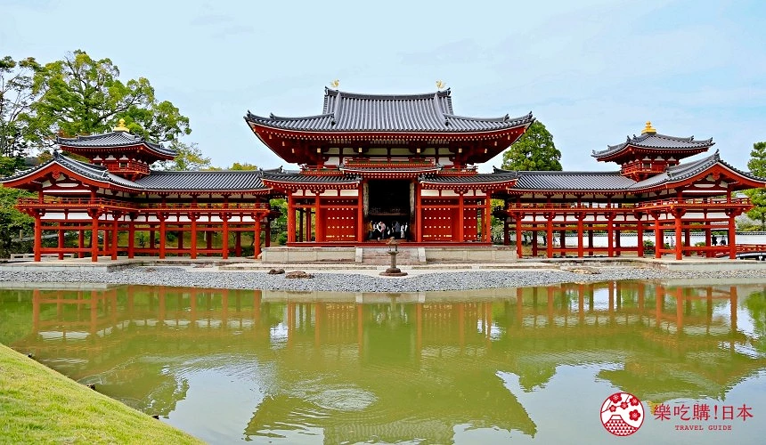 平等院鳳凰堂的紅色木造建築倒映於寧靜池塘中,背景為翠綠庭園與淡藍天空。