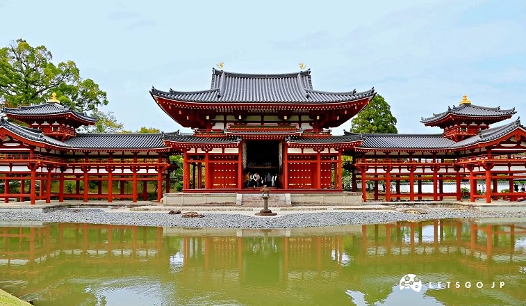 平等院鳳凰堂的紅色木造建築倒映於寧靜池塘中,背景為翠綠庭園與淡藍天空。