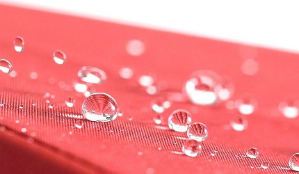 紅色雨傘布料表面水珠凝結滑落,呈現布料的防水與撥水效果
