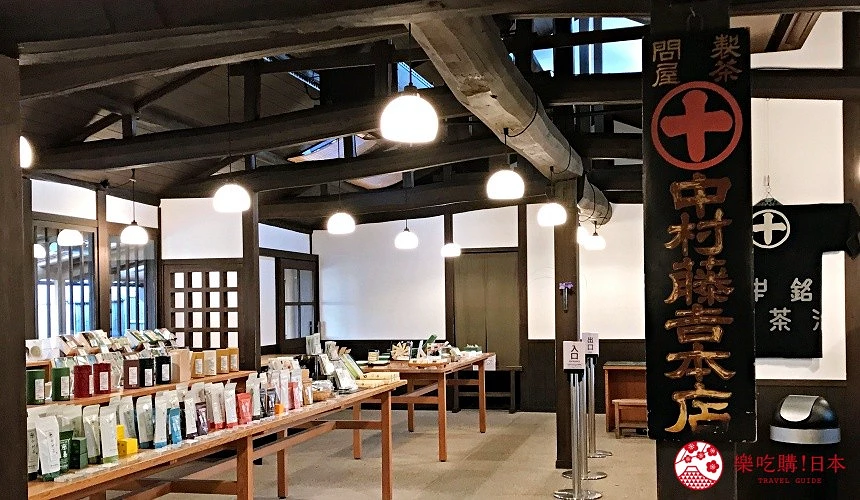 日式古樸室內空間,深色木梁天花板下懸掛圓形吊燈,木桌上陳列各式茶葉包裝與茶具,牆邊掛著黑底白字的店名木招牌。