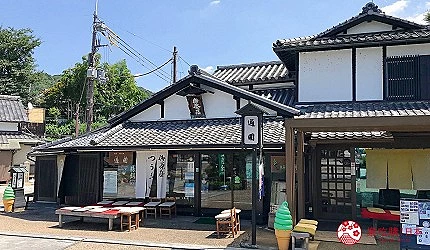 藍天映襯下的傳統日式町屋,白色牆面與深色木樑交錯,瓦頂屋面下門前擺放戶外長椅及霜淇淋造型立牌。