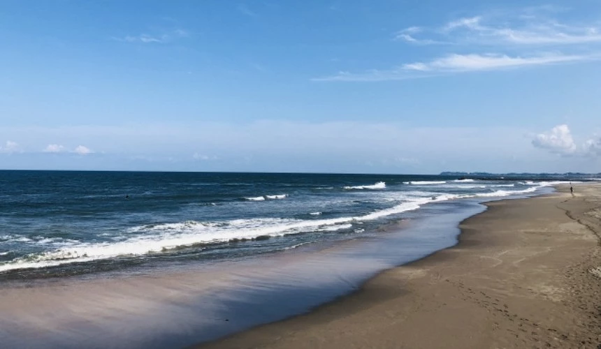 藍天白雲下的海岸線,海浪拍打沙灘延伸至遠方。