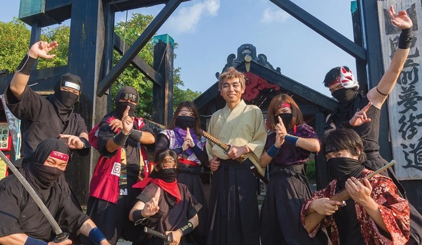 一群身穿忍者服的演員圍在中間持刀男子,背景有古風街道入口木架