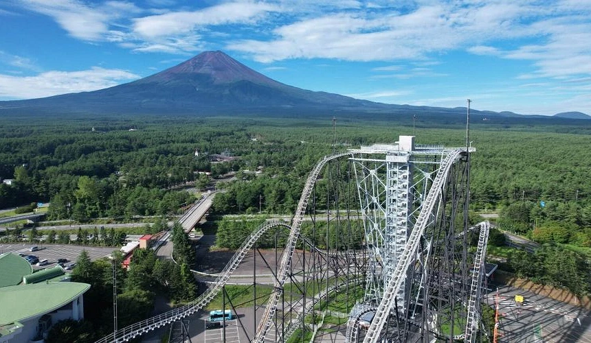 富士急樂園雲霄飛車俯瞰景色,前景為大型遊樂設施,遠方可見富士山與遼闊森林