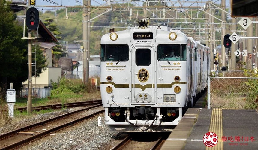 白色JR九州「雙星4047」觀光列車駛入月台,車頭飾有金色星星標誌,兩側可見鐵軌、月台邊緣及訊號燈與架空電纜