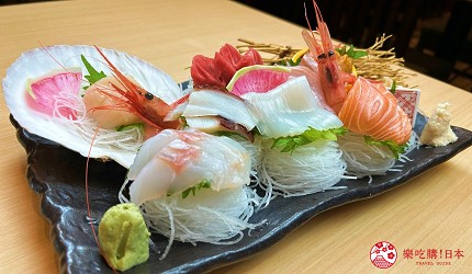 黑色長盤盛放生魚片拼盤，有蝦子、鮭魚、花枝與其他魚片