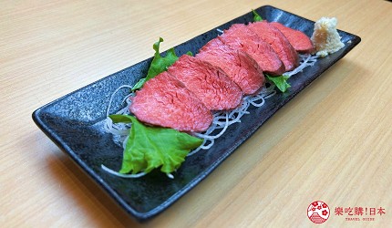 黑色長盤盛放多片生牛肉片，搭配蘿蔔絲與紫蘇葉