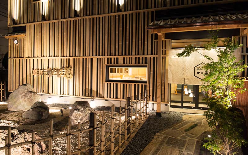 店面入口,木格柵牆與碎石造景,門口掛日文暖簾