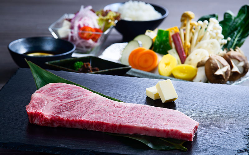 石板上一塊生和牛牛排,旁有蔬菜、白飯與沙拉