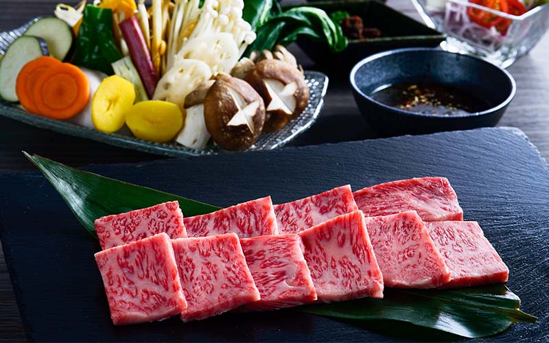石板竹葉上擺放油花牛肉片,旁有蔬菜與沾醬