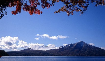 北海道支笏湖秋季景色,湖畔紅葉映襯遠方雪山與碧藍湖水,風光清澈壯麗