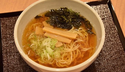 一碗日式拉麵特寫，湯頭呈現金黃色澤，上面放有叉燒肉片、蔥花和海苔，麵條浸泡在濃郁的湯汁中