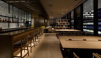 レム東京京橋飯店內的現代化餐廳空間，採用深色木質裝潢和工業風設計，設有開放式廚房和吧台座位，營造時尚都會用餐氛圍