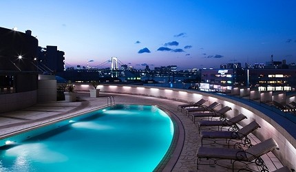 グランドニッコー東京台場飯店的外觀夜景，可見飯店建築與周圍台場地區的現代化建築群，遠方東京市區燈火閃爍，展現東京灣畔的都市夜景