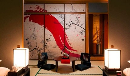 充滿日式風情的和室客房,設有榻榻米地板、圓形茶几與兩張坐墊椅,拉門上繪有紅色筆刷與梅花圖樣,展現濃厚的日本藝術美感