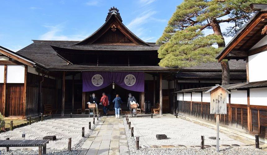 高山陣屋入口主棟,木造建築前方鋪設砂石庭院,旅客從懸掛紫色布幔的入口進入參觀,展現江戶時代官署的歷史風貌