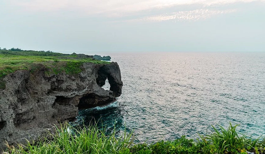 「萬座毛」,其著名的象鼻狀石灰岩斷崖矗立於碧藍大海中,斷崖頂端是一片廣闊的翠綠草地,在柔和光線映照下展現出壯闊的海岸自然奇觀。