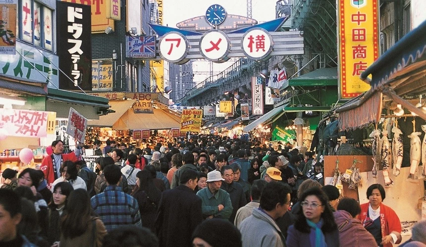 熱鬧的阿美橫丁商店街景象，街道上擠滿購物人潮，兩旁商店招牌密集，充滿傳統日本市場的熱鬧氛圍
