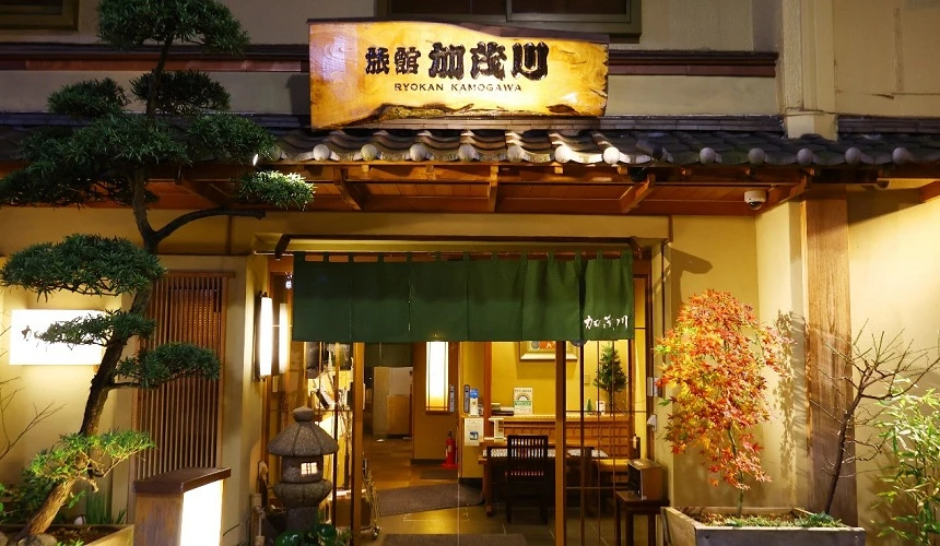 旅館加茂川的傳統日式入口，木質建築搭配暖色調燈光，門口掛有日文招牌，展現典型的日式旅館風格