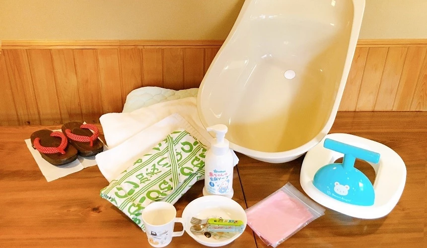 旅館提供的各種嬰兒用品和備品，包含嬰兒洗澡盆、毛巾、護理用品等，擺放在木質地板上供住客使用