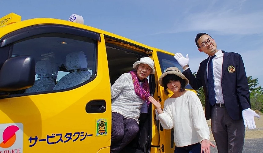 鳥取觀光服務計程車前,多名旅客與司機合影,黃色計程車車身印有「サービス タクシー」字樣