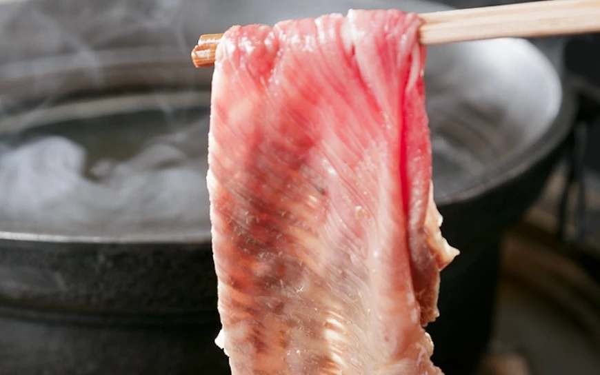 筷子夾起一片牛肉,下方為冒煙的涮涮鍋