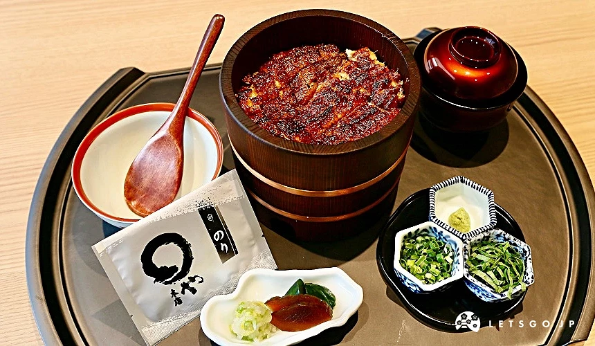 鰻魚飯盛裝於木桶中,托盤上附有茶壺、白碗、木匙、醬菜碟及青蔥海苔配料,旁有寫有「のや」字樣的茶包