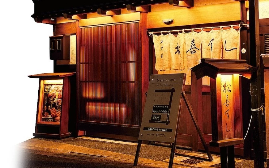 夜晚的松喜壽司店面外觀，散發橘黃色的光