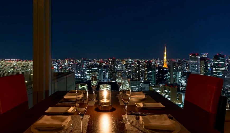 高樓景觀餐廳的夜間用餐桌位,遠處可見點燈的東京鐵塔與城市夜景