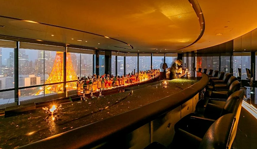 高樓層夜景酒吧,吧台前陳列各式酒瓶,窗外可見東京鐵塔點燈與城市燈火交織的迷人夜色。