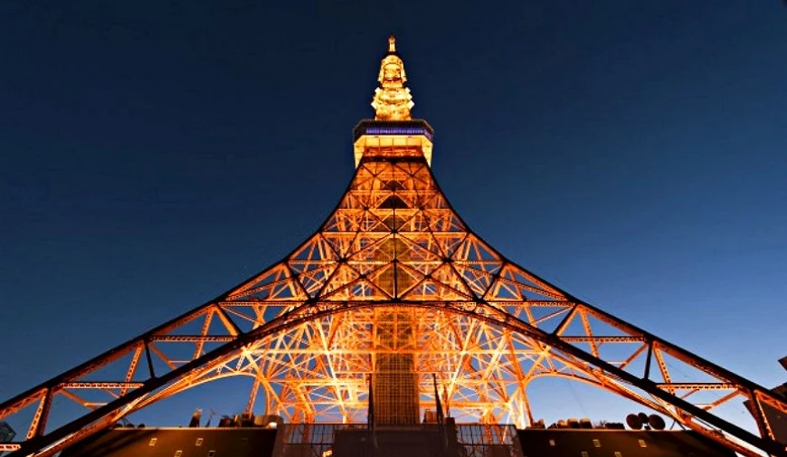 從塔下仰望點燈後的東京鐵塔,橘紅色鋼架在深藍夜空下格外醒目,展現宏偉壯麗的建築美感。