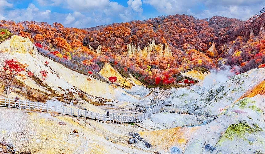 北海道登別溫泉地獄谷與大湯沼,白色硫磺地形與繽紛紅葉相映,蒸氣瀰漫營造奇幻景致