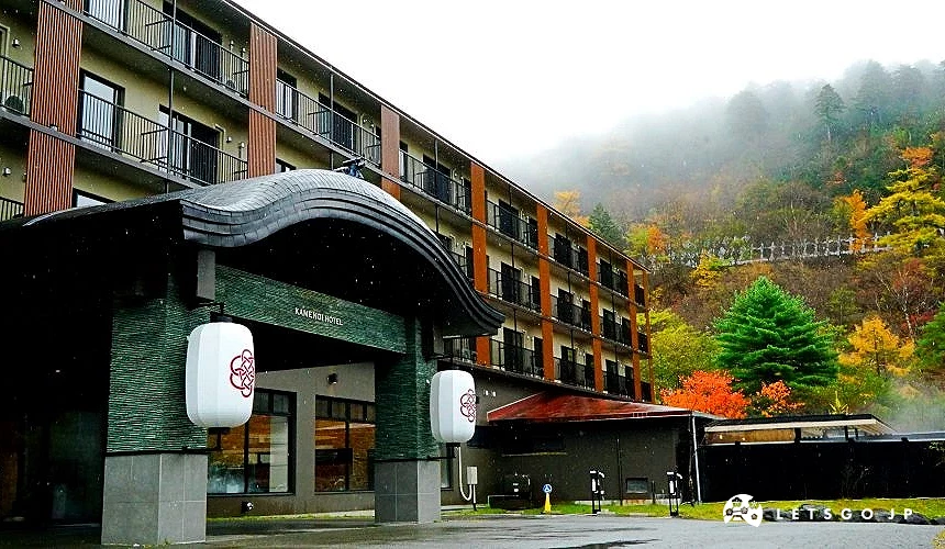 鬼怒川溫泉地區的溫泉旅館外觀,建築前方可見傳統燈籠,背景為被秋季山林與薄霧包圍的自然景色