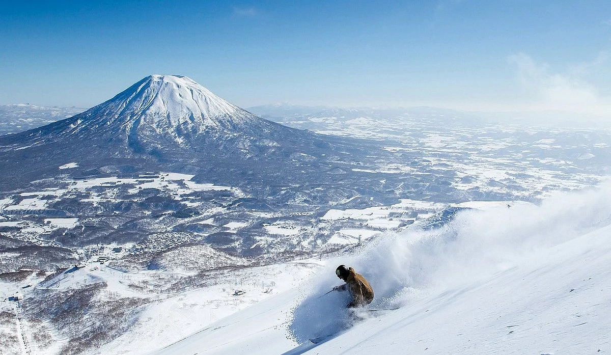 雪場中有人正在滑雪揚起雪,背景為雪山