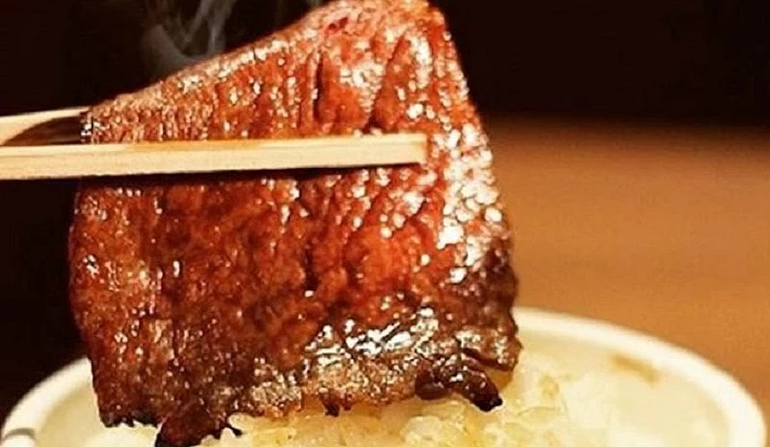 一片剛烤好、刷上醬汁的深褐色燒肉片放在香噴噴的白飯上。