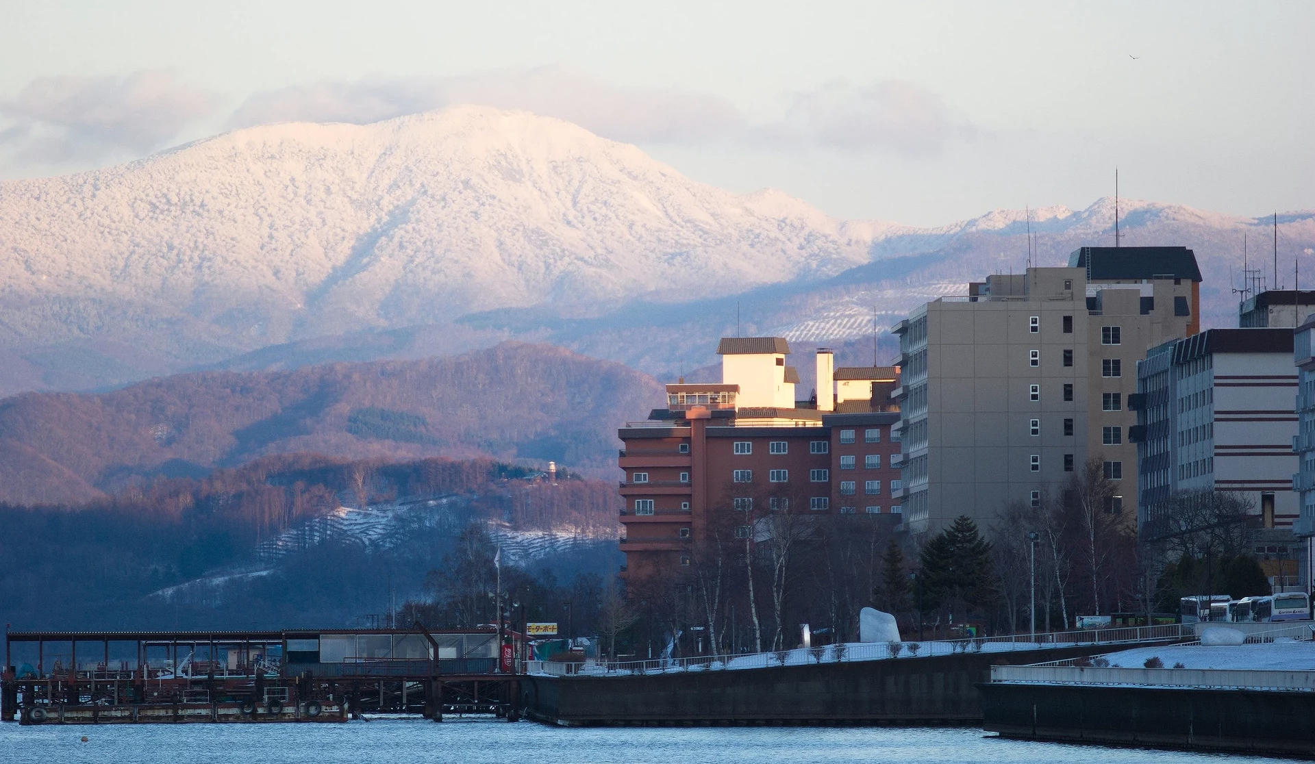 洞爺湖溫泉街冬季景色,湖畔飯店林立,背景為覆雪山巒與冬日天空