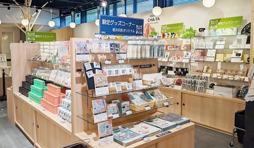 SNOOPY Village 輕井澤店內的限定商品專區,木質貨架上整齊陳列著各式史努比主題的文具、生活雜貨與禮盒。上方掛著藍色與綠色的「輕井澤店限定商品」告示牌,整體空間明亮且充滿童趣氛圍