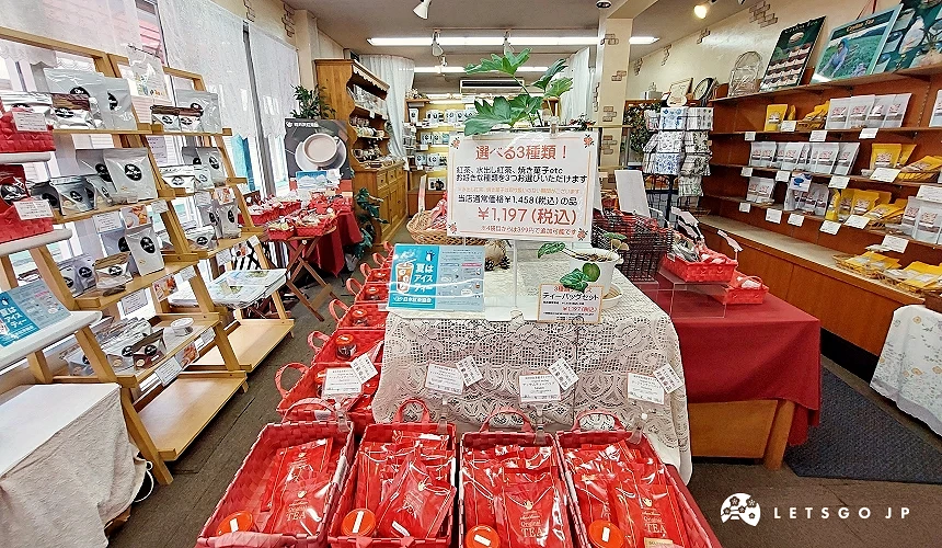 輕井澤紅茶館 (Sun Beam) 的店內環境,桌上整齊擺放著紅色的茶包禮籃,上方設有「任選 3 種類」的優惠海報,價格標示為 1,197 日圓(含稅)。牆邊貨架陳列著各式原創紅茶與精緻茶具組合。